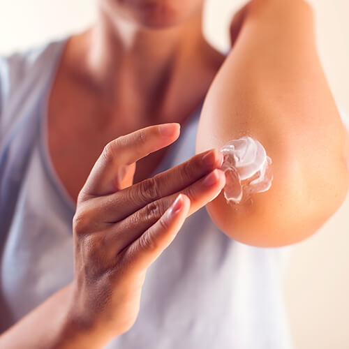 A woman applying lotion to her elbow that could contain glycolic acid for dry skin