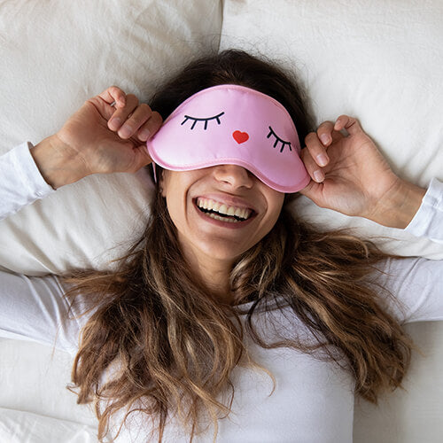 A woman with a sleep mask on waking up after her skin regenerates at night