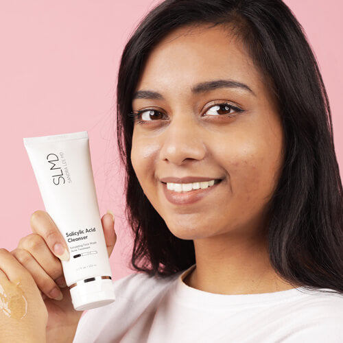 A woman holding SLMD Skincare Salicylic Acid Cleanser, one of Dr. Pimple Popper's skincare essentials
