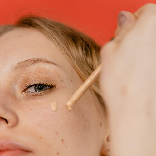 A woman applying concealer to acne that can be treated with Spot Check Acne Patches by SLMD Skincare