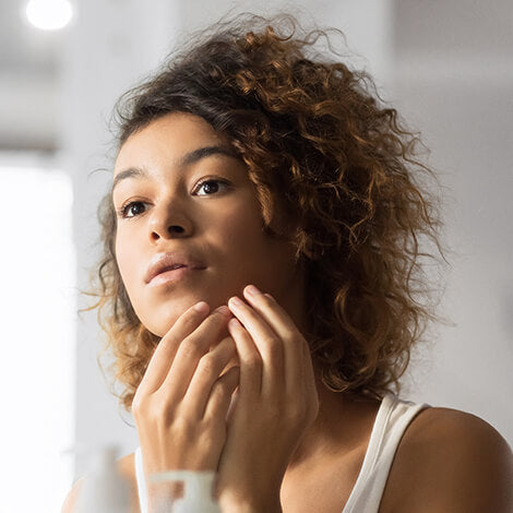 A woman examining her hormonal acne in the mirror