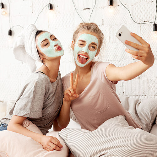 Women taking selfies with facial masks on as part of Cleanse, Treat, Moisturize skincare philosophy