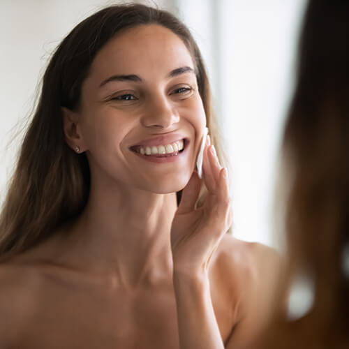 A smiling woman applying skincare possibly glycolic acid