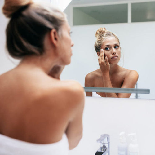 A woman examining her oily skin in the mirror