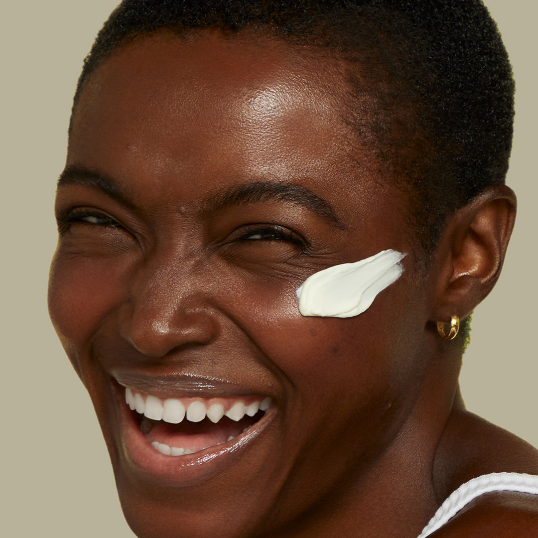 A model smiling as she's about to reapply her SLMD Skincare sunscreen