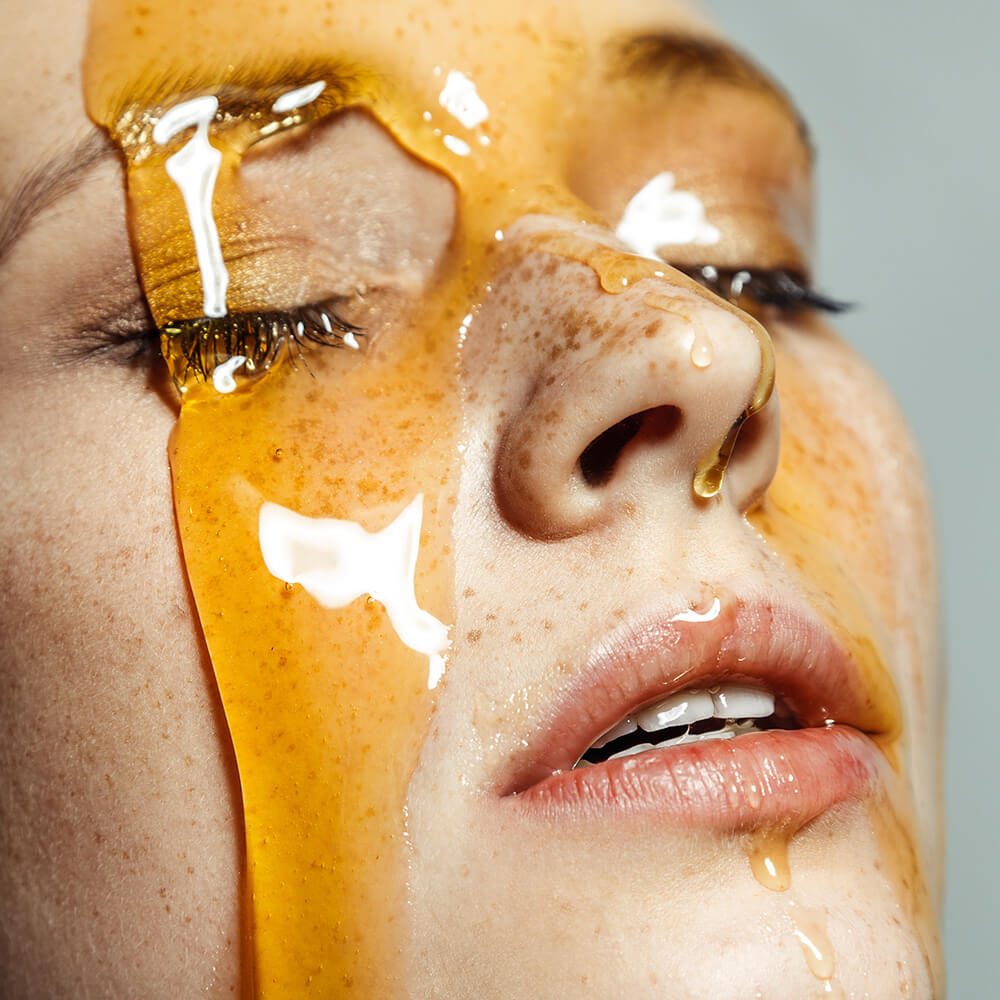 A woman with honey flowing down her face representing the idea of clean beauty