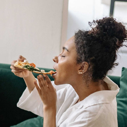 Photo of a woman eating greasy pizza, which may contribute to acne breakouts, says Dr. Pimple Popper