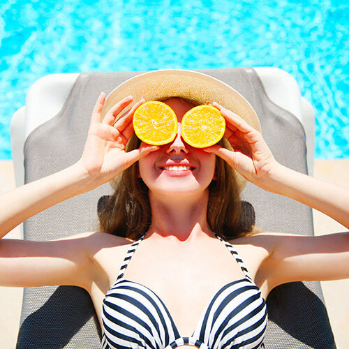 A woman by the pool with oranges that contain antioxidant vitamin c to protect from UV damage
