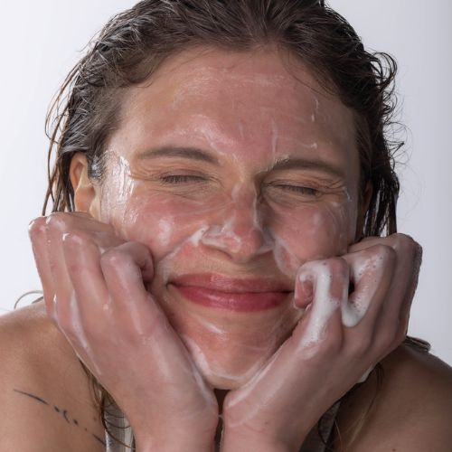 A photo of a smiling woman with SLMD Salicylic Acid Cleanser lathered on her face