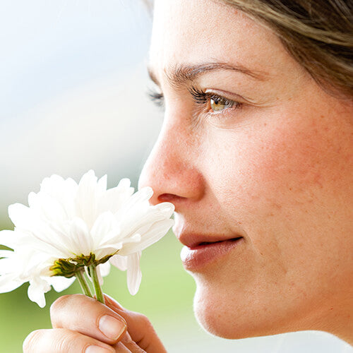 A woman with healthy skin smelling a springtime flower 