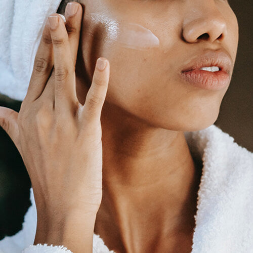 A woman with glowing skin applying brightening product like retinol serum by SLMD Skincare