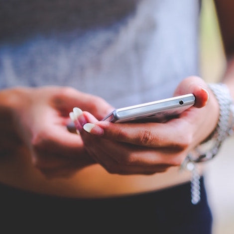 A closeup photo of a woman looking at her cellphone which emits skin-damaging blue light