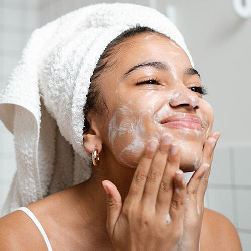 A photo of a woman smiling as she's cleansing her face