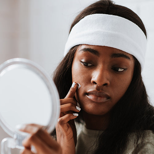 A young woman applying skincare in mirror similar to Retinol Serum by SLMD Skincare